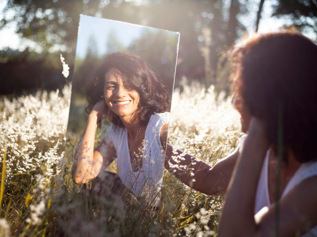 Midlife woman looking at herself in a mirror in a field and smiling at herself
